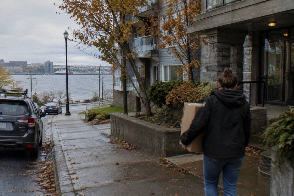 A person carrying a moving box toward a low-rise condo building in Halifax